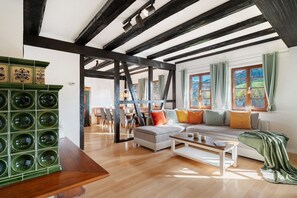 Ein geräumiges Wohnzimmer mit freiliegenden Holzbalken, einer Couch mit bunten Kissen und einem grünen Schrank.