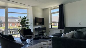 Ein modernes Wohnzimmer mit Sofa, Sessel, Fernseher und einer Topfpflanze.