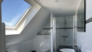 Ein modernes Badezimmer mit Oberlicht, einer Badewanne, einer Dusche und einem Waschbecken.