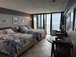 Ein Hotelzimmer mit zwei Betten, einem kleinen Tisch, einem Stuhl und einem Balkon mit Blick.