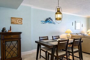 A dining area with a table and chairs, a decorative wall piece, a lamp, and a sofa in the background. - Oceanfront Luxury Condo Million-Dollar Views (Ponce Inlet)