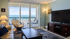 Ein Wohnzimmer mit Fernseher, einer Couch, einem Sessel und einem Balkon mit Meerblick.