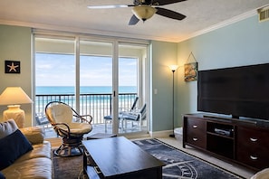 Ein Wohnzimmer mit Fernseher, einer Couch, einem Sessel und einem Balkon mit Meerblick.