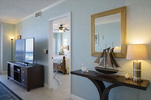 A hotel room with a TV, a bed, a ceiling fan, a desk with a lamp, and a large mirror. - Oceanfront Luxury Condo Million-Dollar Views (Ponce Inlet)
