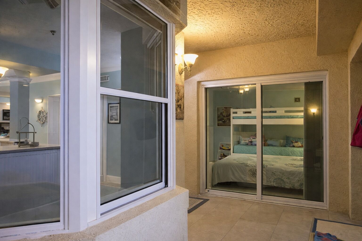 A bedroom with a sliding glass door, a bunk bed, and a small table with a lamp.