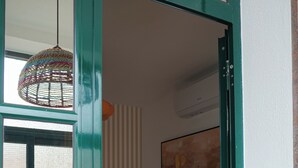 Et værelse med en dør i grøn ramme, et rundt bord med stole, en hængende lampe og en vægmonteret aircondition.
