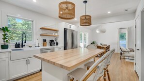 A modern kitchen with white cabinetry, a wooden island, and a dining area with a bench and chairs. - Completely Renovated Modern Hampton Bays Retreat with Brand New Pool,... (Hampton Bays)