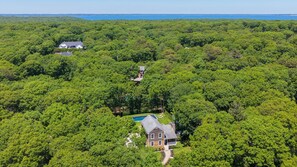 An aerial view of a property surrounded by dense forest, featuring a large house with a swimming pool and a smaller building.