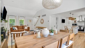 A spacious living area with a wooden dining table, a sofa, and a kitchen in the background.