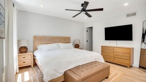 A modern bedroom with a wooden bed, bedside lamps, a ceiling fan, a TV, and a wardrobe.