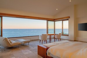 Ein Hotelzimmer mit weitreichendem Meerblick, einem Bett, einer Sitzecke mit Stühlen und einem kleinen Tisch.