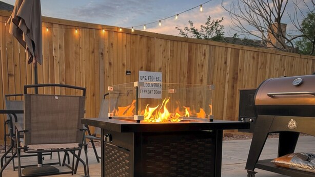 Eine Terrasse mit Feuerstelle, Grill, Gartenmöbeln und einem Holzzaun.