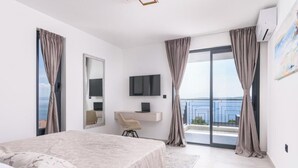 Une chambre moderne avec un lit, un bureau, une télévision et un balcon agrémenté de rideaux.