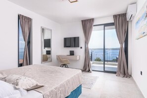 Ein modernes Schlafzimmer mit Bett, Schreibtisch, Fernseher und einem Balkon mit Vorhängen.