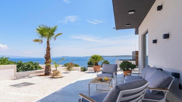 Une terrasse avec des sièges extérieurs, un palmier et une vue sur la mer.