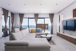 A modern living room with a sectional sofa, a round coffee table, and a large TV mounted on the wall. - Villa Adriatica (Okrug Gornji, Trogir,)