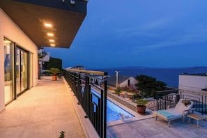 A balcony with a pool, lounge chairs, and a view of the sea. - Villa Adriatica (Okrug Gornji, Trogir,)