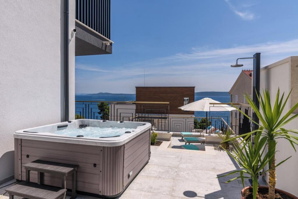 A hot tub on a patio with a view of the sea and buildings in the background.