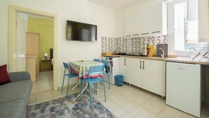 Un espacio habitable compacto con kitchenette, una zona de comedor con mesa y sillas, un sofá y una televisión.