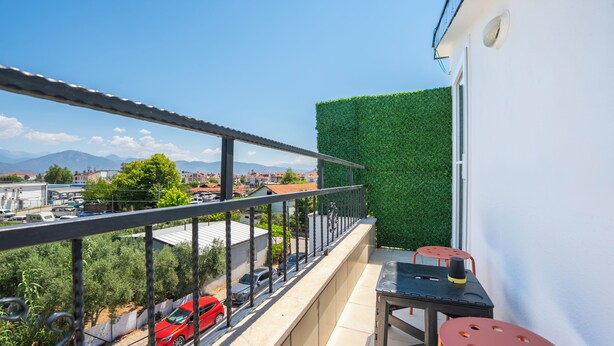 Un balcón con vistas a una calle y edificios, una pared verde y una mesa con sillas.
