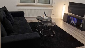 A living room with a black sofa, a small round table, a TV, and a radiator. - Vacation Rental in Lüchtringen (Höxter)