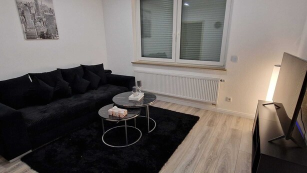 A modern living room with a black sofa, a round coffee table, and a TV stand. - Vacation Rental in Lüchtringen (Höxter)