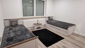 A bedroom with two beds, a small bedside table, a radiator, and a window with blinds. - Vacation Rental in Lüchtringen (Höxter)