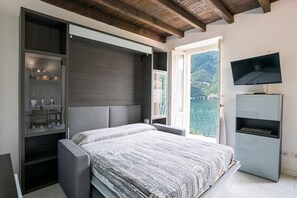 Ein Schlafzimmer mit Bett, Regalen, Fernseher und Blick auf eine Berglandschaft.