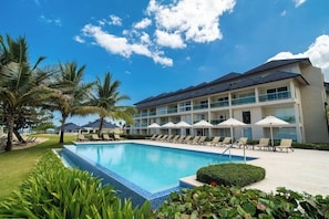 Un hotel con piscina, sillas de descanso, sombrillas y palmeras.