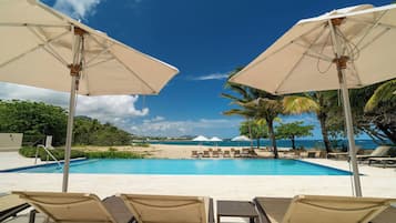 Zona junto a la piscina con sillones de descanso y sombrillas, cielo azul despejado y vistas a la playa y al océano.