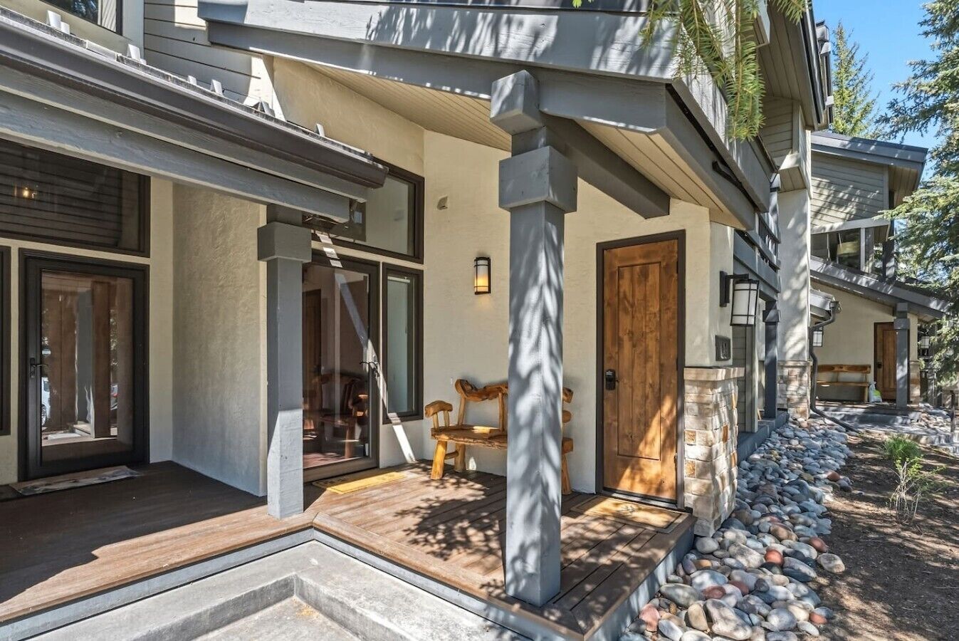 Une maison moderne dotée d’un porche abrité, d’une cheminée en pierre et d’un banc en bois.