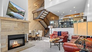 Un salon moderne avec une cheminée, un coin repas, un canapé en cuir et un escalier.