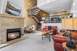 A modern living room with a fireplace, a dining area, a leather sofa, and a staircase. - The Guilded Antler | Ski Access, Hot Tub & Pool (Beaver Creek)