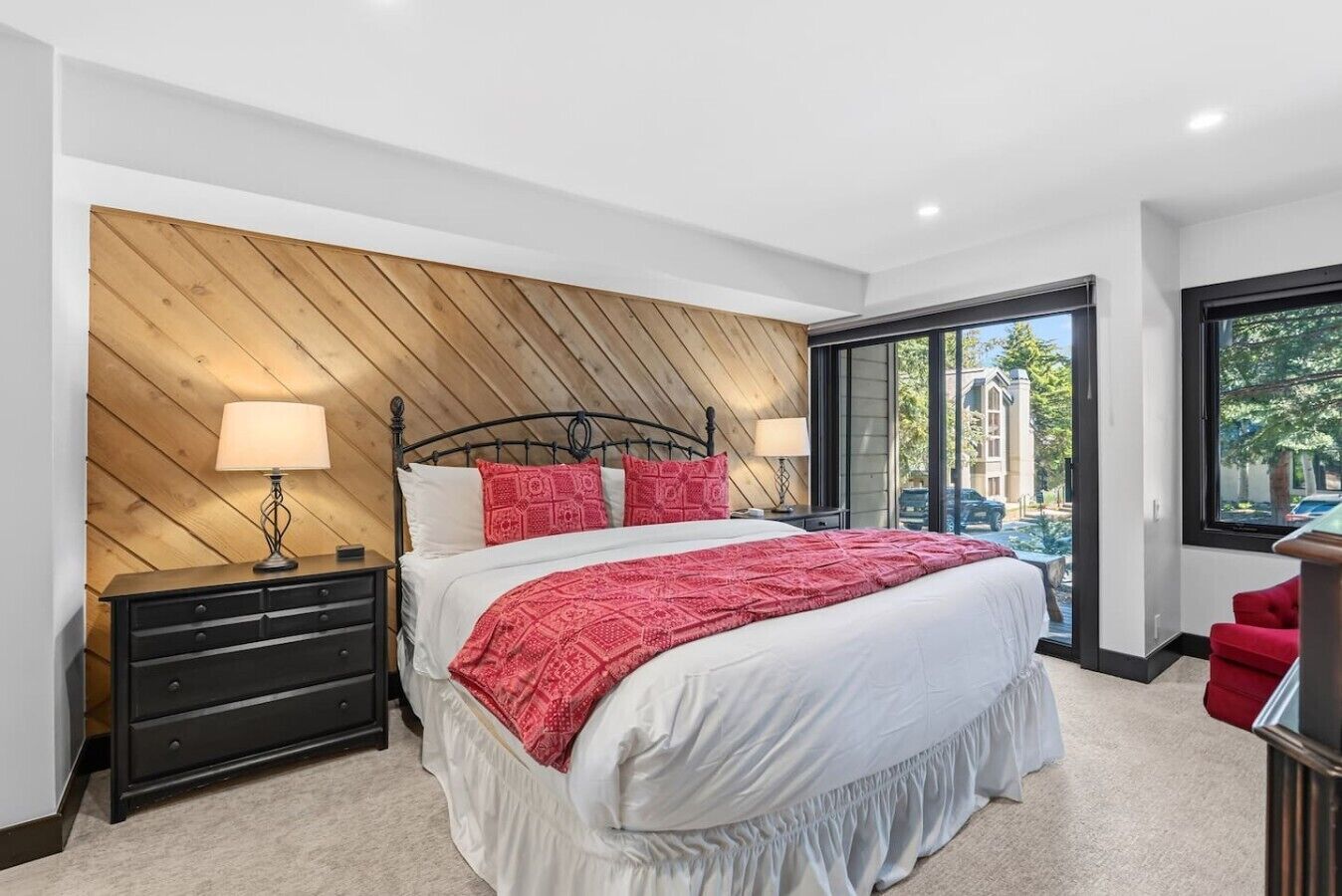 Une chambre à coucher avec un lit, une commode, une fenêtre donnant sur un beau paysage et un fauteuil rouge.