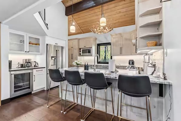 A modern kitchen with white cabinetry, a central island with bar stools, stainless steel appliances, and a wooden ceiling. - The Guilded Antler | Ski Access, Hot Tub & Pool (Beaver Creek)