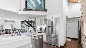 Une cuisine moderne dotée d’appareils électroménagers en acier inoxydable, d’un plan de travail en marbre et d’un escalier menant à l’étage supérieur.