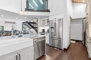 A modern kitchen with stainless steel appliances, a marble countertop, and a staircase leading to an upper level. - The Guilded Antler | Ski Access, Hot Tub & Pool (Beaver Creek)