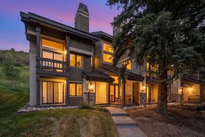 A modern multi-story house with a stone fireplace, large windows, and a well-maintained lawn. - The Guilded Antler | Ski Access, Hot Tub & Pool (Beaver Creek)