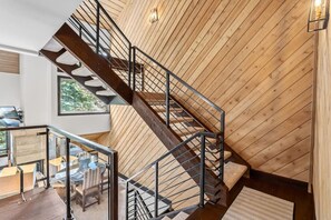 A modern interior with a wooden sloped ceiling, a staircase with metal railings, and a view of a dining area. - The Guilded Antler | Ski Access, Hot Tub & Pool (Beaver Creek)