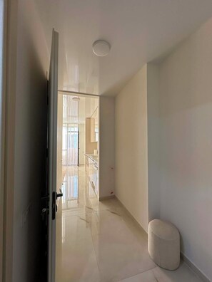 Un couloir avec une porte, un petit pouf rond et un luminaire au plafond.