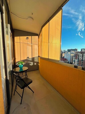 Een balkon met een tafel, stoelen, een bloempot en uitzicht op gebouwen.