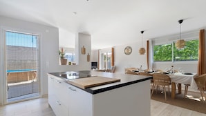 A modern kitchen with a central island, dining area with chairs, and a large window with curtains. - 4-Bedroom Villa with Private Pool & Spa for 8, Carquefou/Nantes (Carquefou)