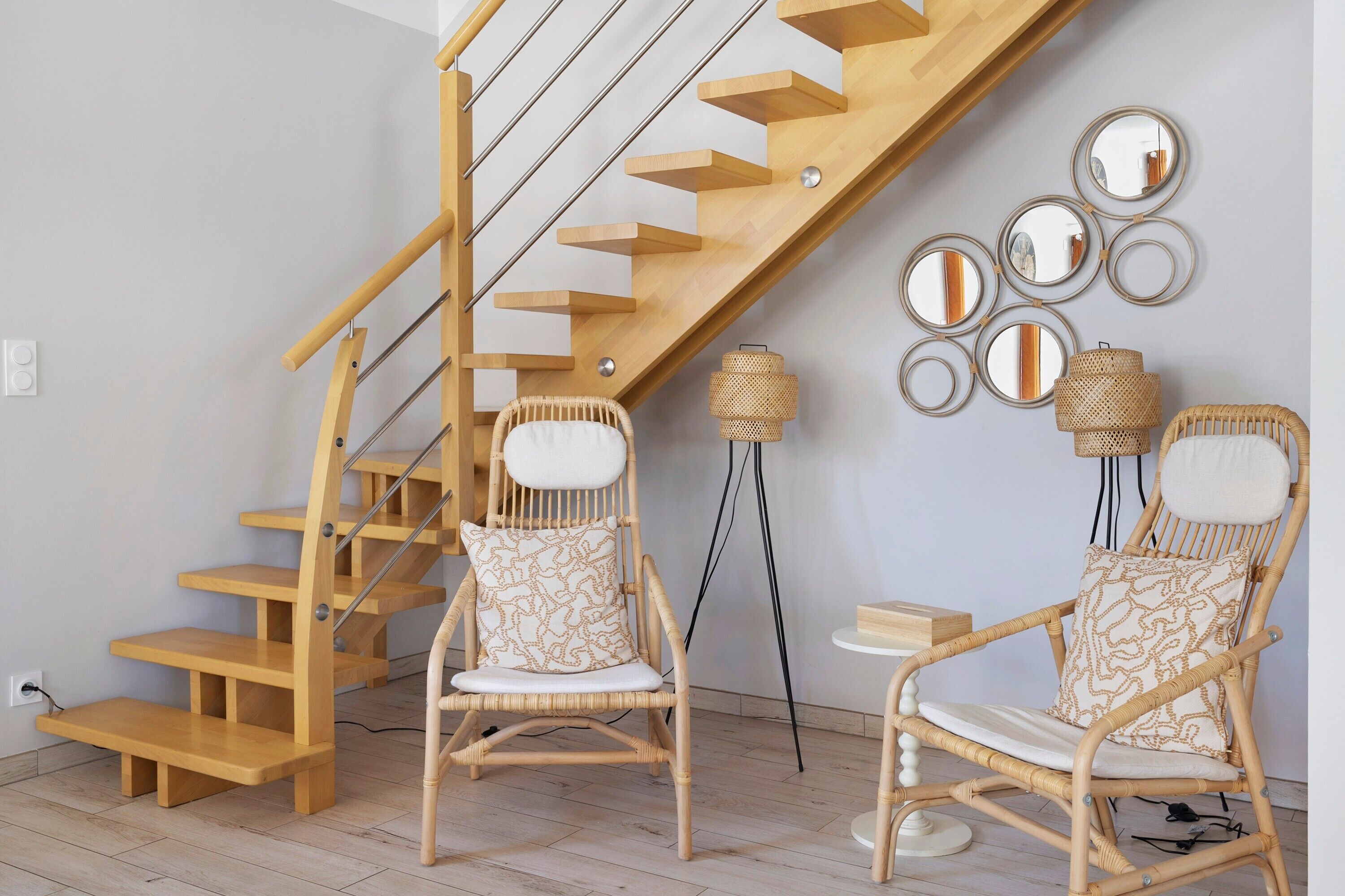 A staircase with wooden steps and a handrail, two wicker chairs with patterned cushions, and wall-mounted mirrors.