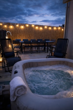 Un jacuzzi con una toalla, asientos exteriores e iluminación de luces colgantes.