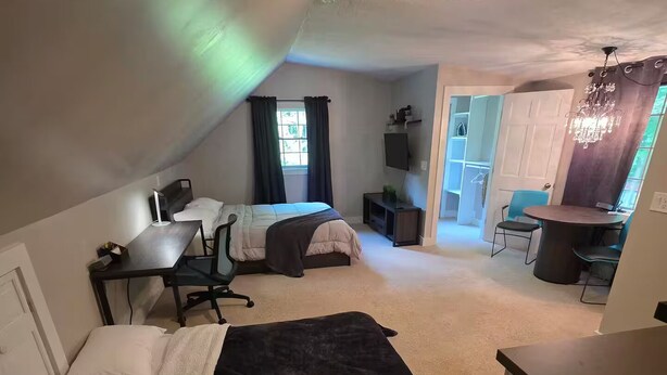 Habitación pequeña con dos camas, un escritorio, una silla, un televisor y una zona de comedor con sillas y una mesa.