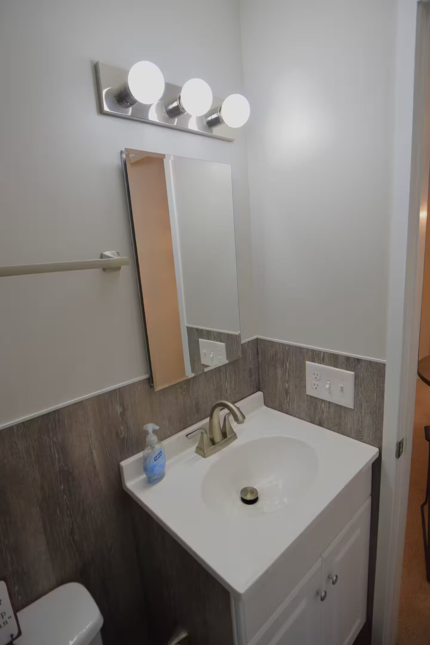 Un bagno con un lavandino bianco, uno specchio e un porta asciugamani.