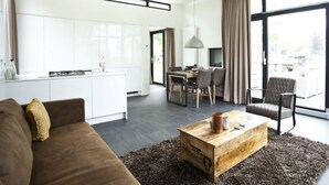 A modern living space with a sofa, a wooden coffee table, a dining area, and a kitchen. - Cube Maximaal 4 (Halfweg)
