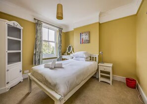 Une chambre à coucher comprenant un lit, une table de chevet, une commode, une armoire et une fenêtre avec des rideaux.