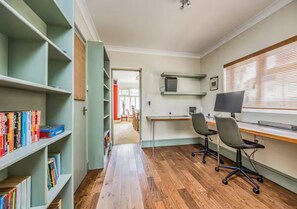 Een kamer met een lange houten vloer, een bureau met twee stoelen en boekenkasten vol boeken.