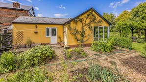 Ein gelbes Haus mit Garten, einer weißen Tür und einem Fenster.